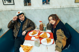 Male and female sitting at a talbe with slices of pizza on it.